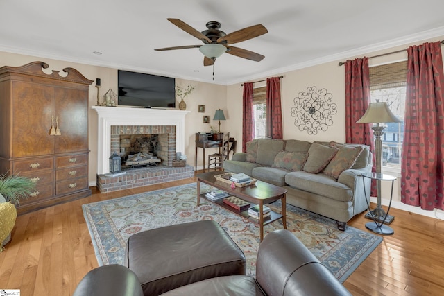 living area with ceiling fan, ornamental molding, a brick fireplace, and light wood-style floors