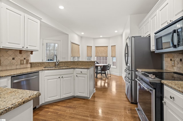 kitchen with white cabinets, wood finished floors, light stone countertops, stainless steel appliances, and a sink