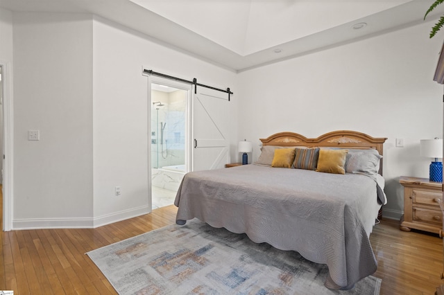 bedroom with a barn door, ensuite bath, wood finished floors, and baseboards