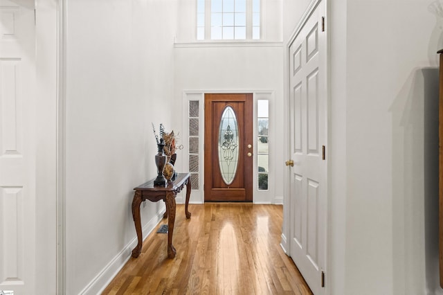 entryway featuring a towering ceiling, light wood finished floors, and baseboards