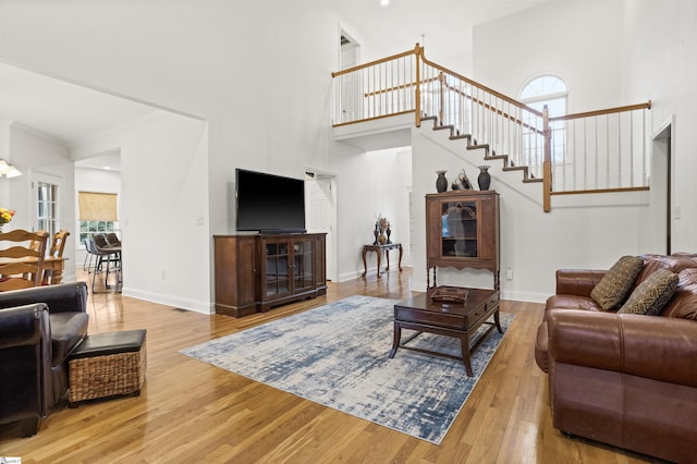 living room featuring a towering ceiling, stairway, ornamental molding, wood finished floors, and baseboards