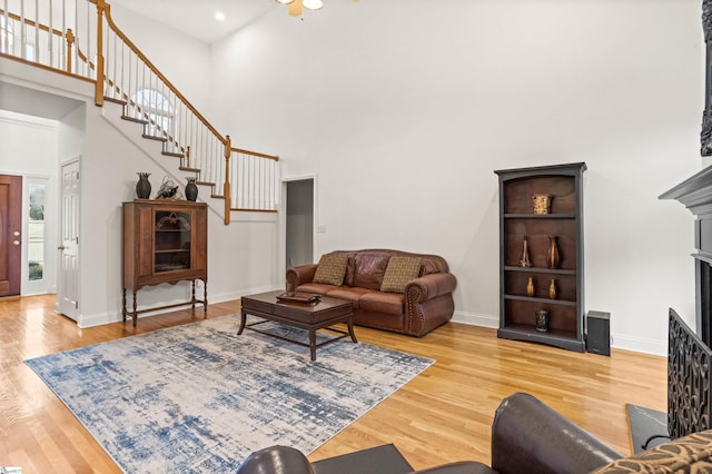 living area featuring baseboards, stairway, wood finished floors, a high ceiling, and a fireplace