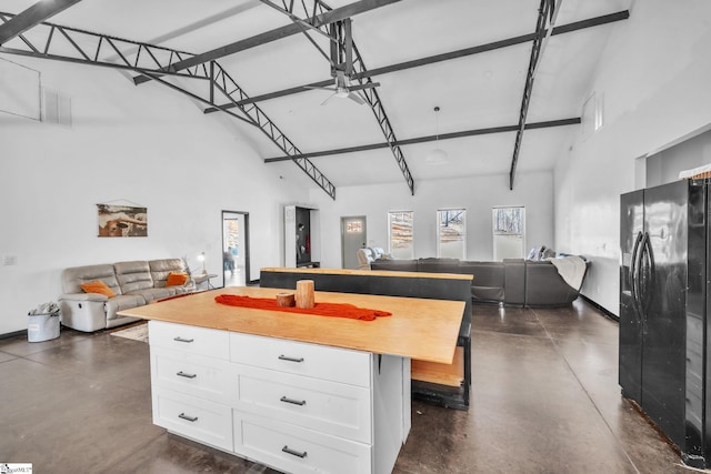 kitchen with concrete flooring, open floor plan, white cabinets, and black fridge