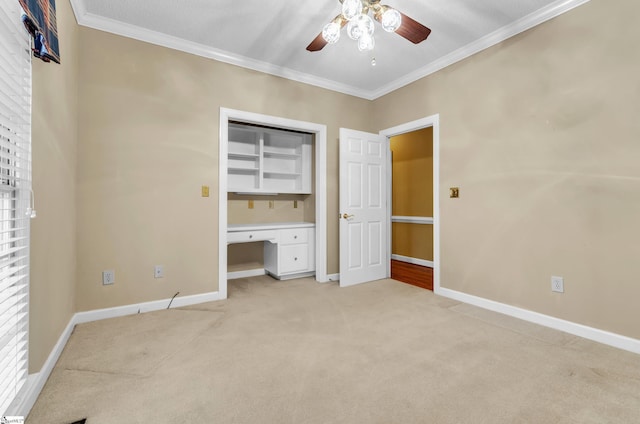 unfurnished bedroom featuring light carpet, baseboards, a ceiling fan, built in study area, and crown molding