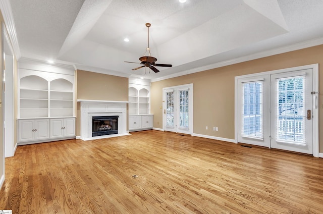 unfurnished living room featuring light wood finished floors, baseboards, a tray ceiling, and a high end fireplace