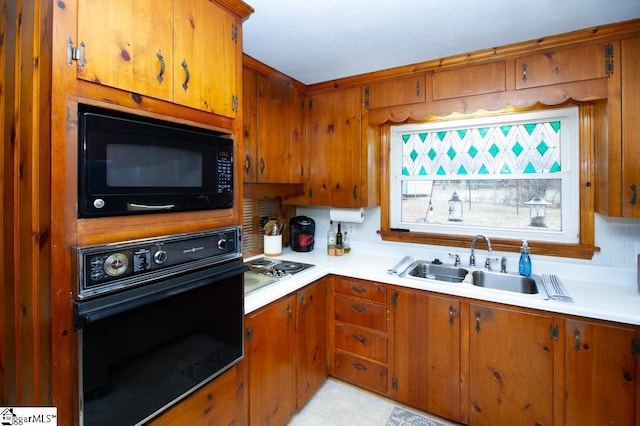 kitchen featuring a sink, black appliances, light countertops, and brown cabinets