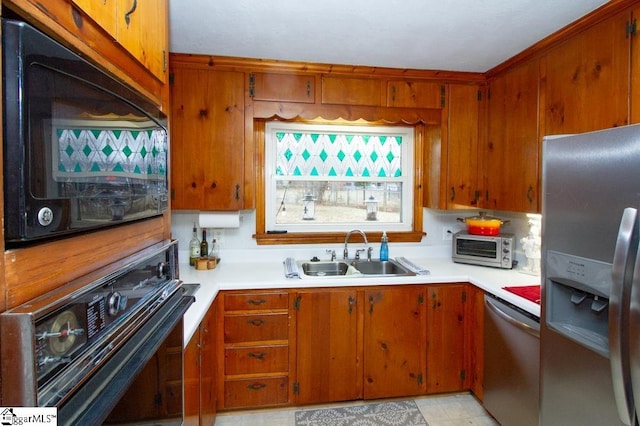 kitchen featuring a toaster, brown cabinetry, light countertops, black appliances, and a sink