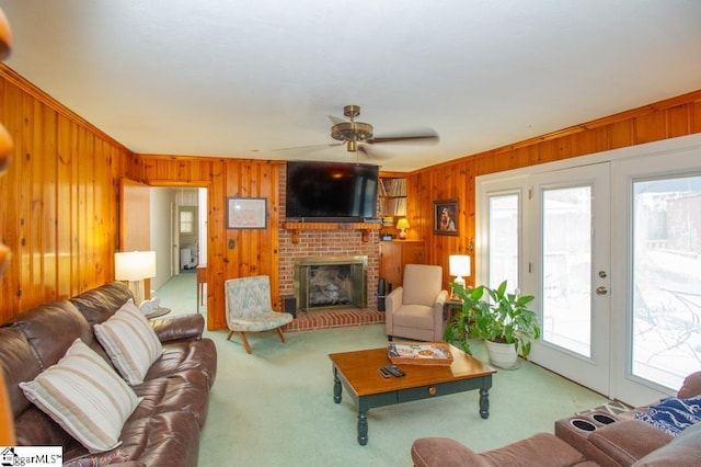 carpeted living area featuring wood walls, ceiling fan, ornamental molding, french doors, and a brick fireplace