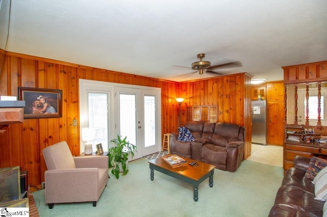 living room with a wealth of natural light, light carpet, ceiling fan, and wood walls