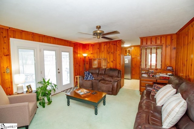 living area with wooden walls, a ceiling fan, and light colored carpet