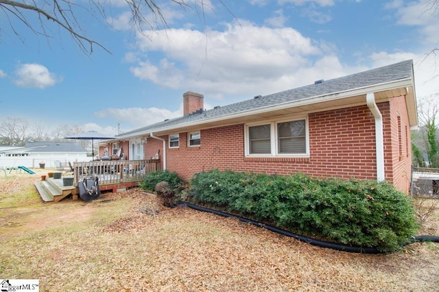 back of property with a deck, brick siding, a chimney, and fence