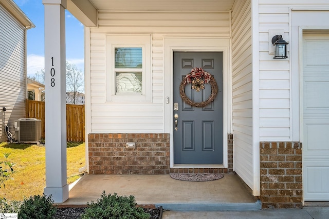 property entrance featuring a garage, central AC unit, fence, and brick siding