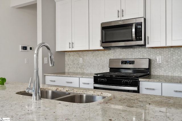 kitchen featuring light stone counters, stainless steel appliances, a sink, white cabinetry, and tasteful backsplash