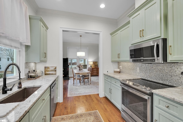 kitchen with light stone counters, crown molding, hanging light fixtures, appliances with stainless steel finishes, and a sink