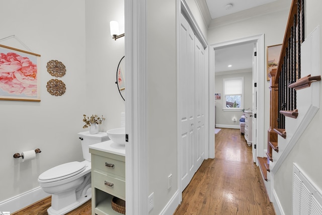 half bath featuring visible vents, vanity, toilet, and wood finished floors