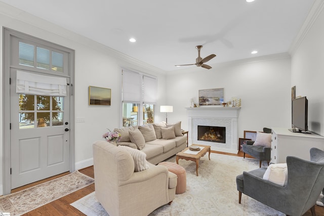 living room with light wood-style floors, a warm lit fireplace, ornamental molding, and recessed lighting