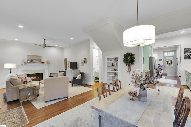 dining room with a lit fireplace, ornamental molding, light wood-type flooring, and recessed lighting