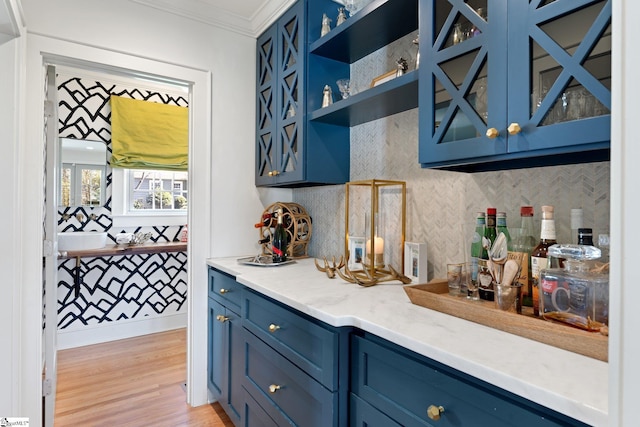 bar with a bar, ornamental molding, light wood-type flooring, and tasteful backsplash