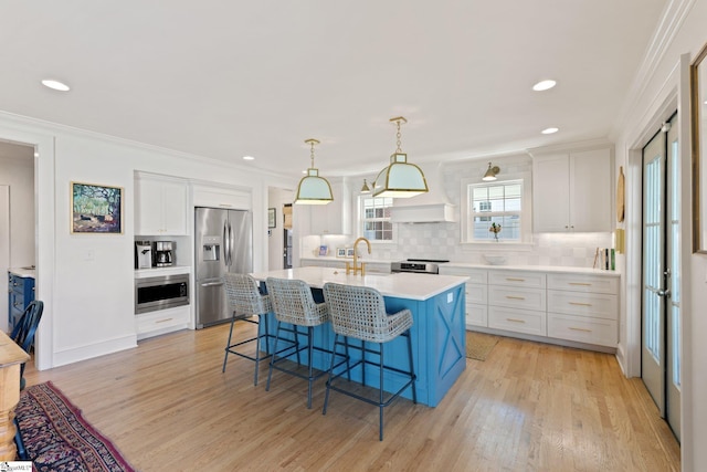 kitchen with a kitchen island with sink, stainless steel appliances, a kitchen breakfast bar, white cabinets, and light countertops