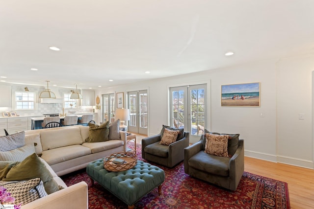 living area featuring french doors, recessed lighting, ornamental molding, light wood-type flooring, and baseboards