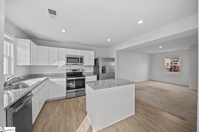 kitchen with a center island, stainless steel appliances, open floor plan, white cabinetry, and a sink