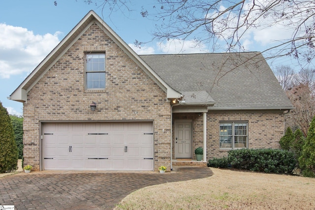 traditional home featuring a garage, brick siding, decorative driveway, and a shingled roof