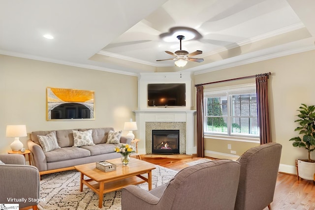 living area featuring light wood-type flooring, baseboards, a raised ceiling, and crown molding