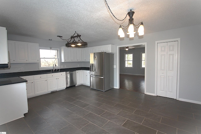 kitchen featuring appliances with stainless steel finishes, dark countertops, white cabinets, and hanging light fixtures