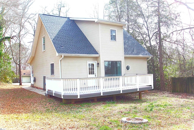 rear view of house with a deck, a yard, a shingled roof, and fence