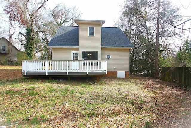 rear view of house with a yard, a shingled roof, a wooden deck, and fence