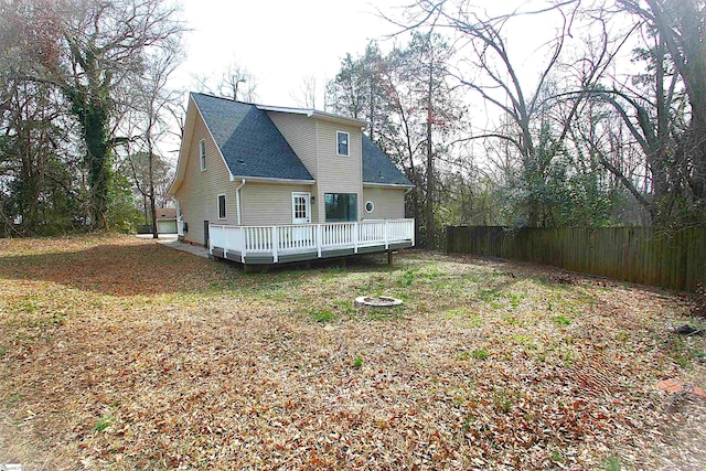 back of property with a deck, roof with shingles, and fence