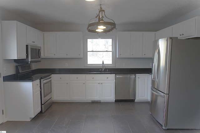 kitchen featuring white cabinets, dark countertops, decorative light fixtures, stainless steel appliances, and a sink