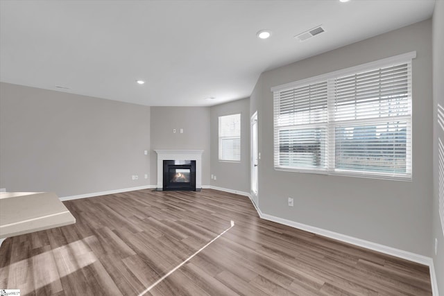 unfurnished living room featuring baseboards, visible vents, a fireplace with flush hearth, wood finished floors, and recessed lighting