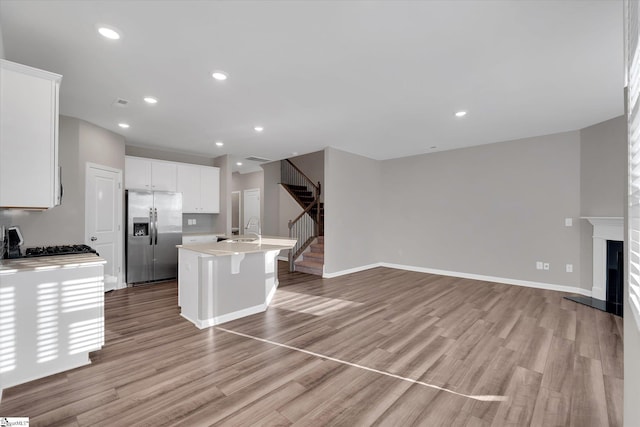 kitchen with stainless steel fridge, a center island with sink, light countertops, and open floor plan