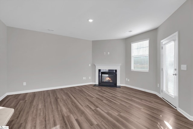 unfurnished living room with wood finished floors, a fireplace with flush hearth, visible vents, and baseboards