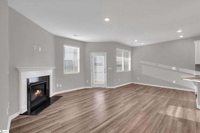 unfurnished living room with light wood-style floors, a glass covered fireplace, visible vents, and baseboards