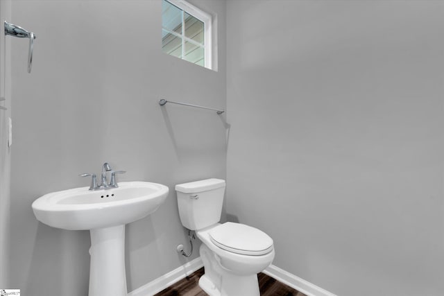 half bath with a sink, wood finished floors, toilet, and baseboards