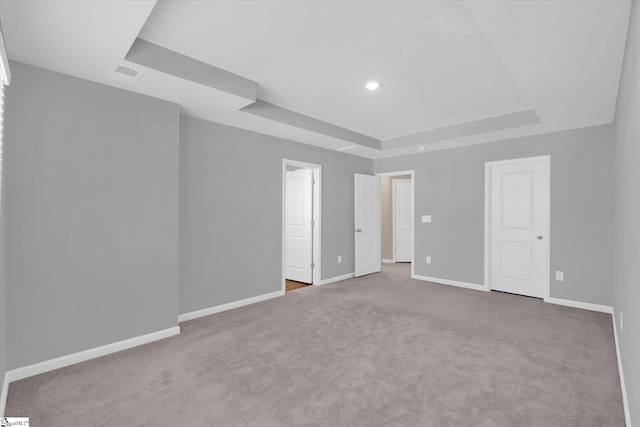 unfurnished bedroom with recessed lighting, light colored carpet, visible vents, baseboards, and a tray ceiling