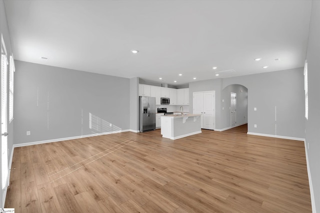 unfurnished living room featuring light wood finished floors, baseboards, arched walkways, a sink, and recessed lighting