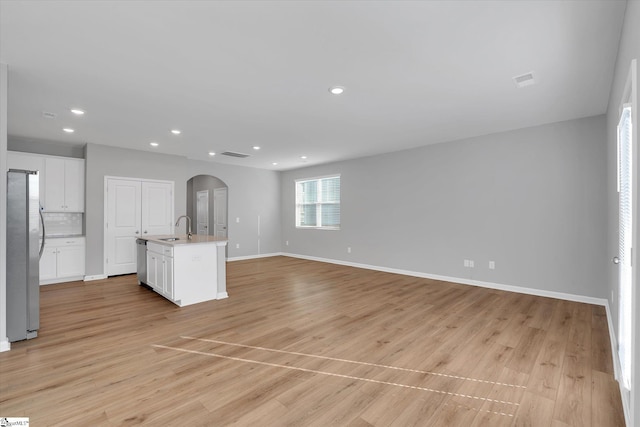 unfurnished living room featuring baseboards, arched walkways, light wood-style flooring, a sink, and recessed lighting