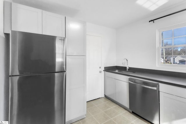 kitchen featuring light tile patterned floors, white cabinets, dark countertops, appliances with stainless steel finishes, and a sink