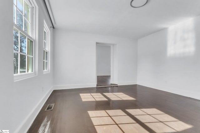 spare room with dark wood-style flooring, visible vents, and baseboards