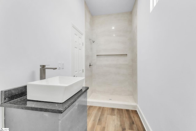 bathroom featuring wood finished floors, a stall shower, a sink, and baseboards