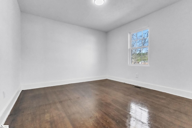 empty room featuring dark wood finished floors, visible vents, and baseboards