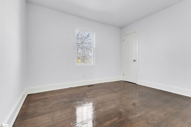 empty room featuring dark wood-type flooring, visible vents, and baseboards