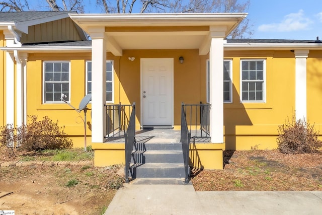 entrance to property featuring a shingled roof and stucco siding