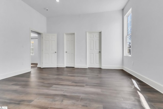 unfurnished bedroom with dark wood-style flooring, multiple windows, and baseboards