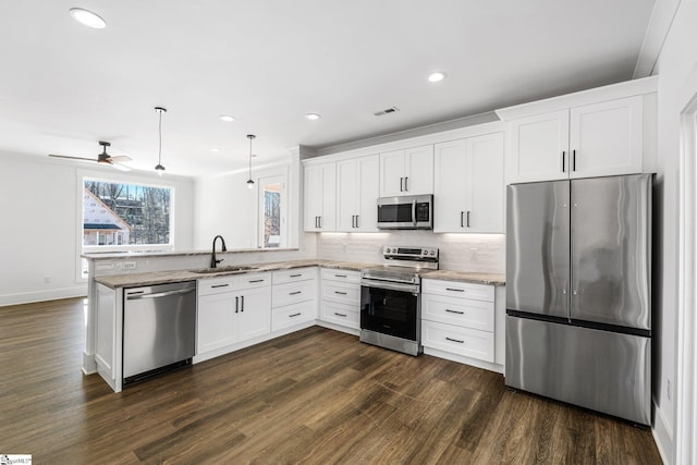 kitchen featuring dark wood-style floors, stainless steel appliances, hanging light fixtures, white cabinetry, and a sink