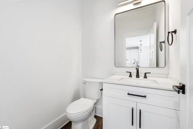 half bathroom featuring baseboards, vanity, toilet, and wood finished floors