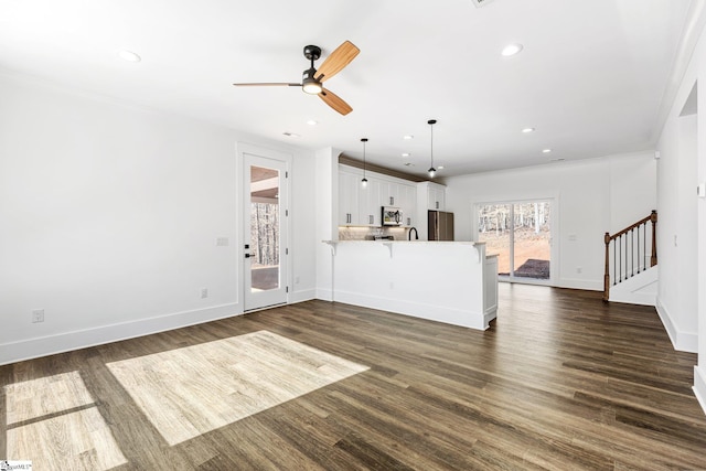 unfurnished living room with dark wood-type flooring, recessed lighting, stairway, and baseboards